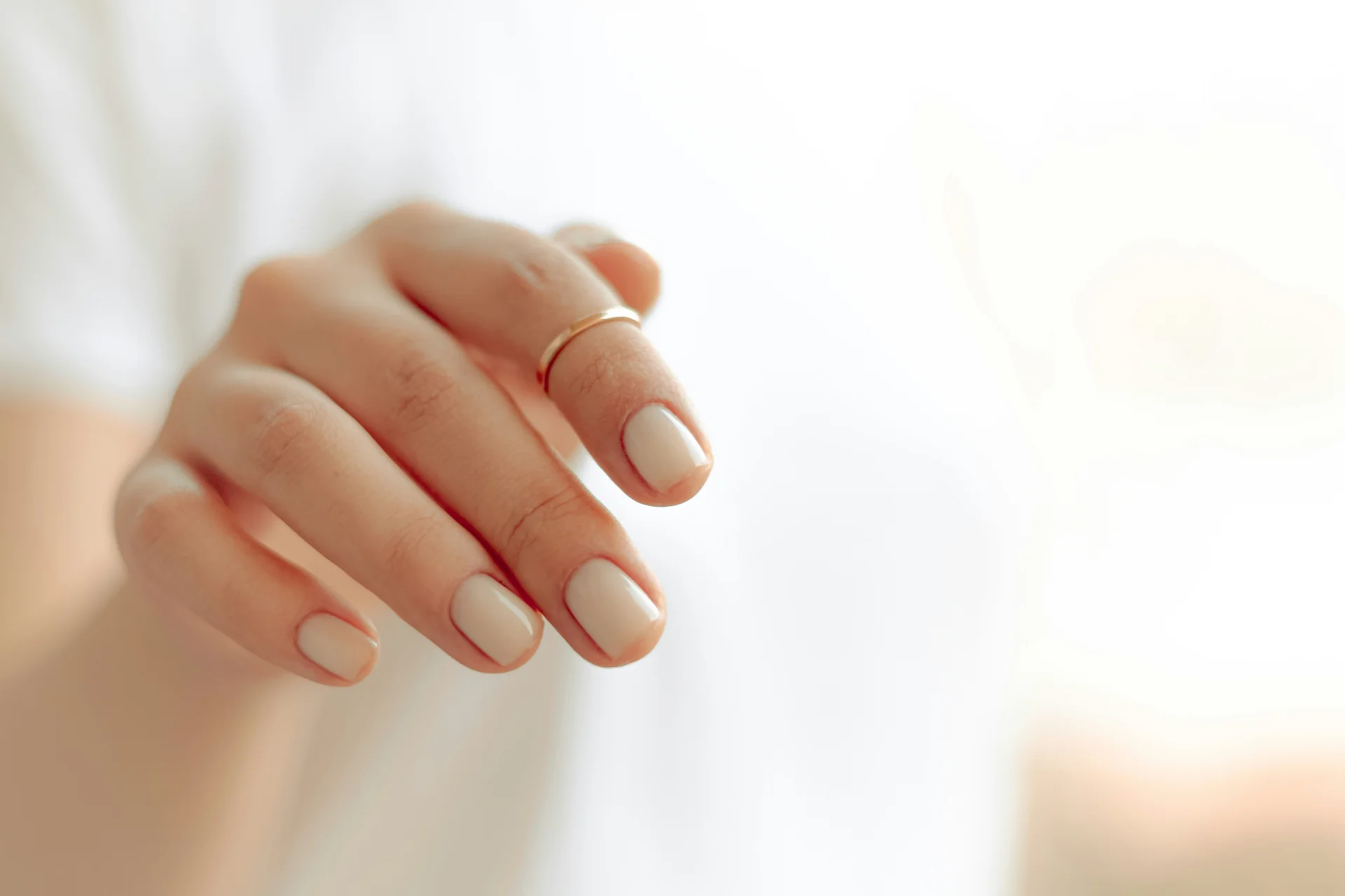 Zbliżenie na dłoń z eleganckim, białym manicure, prezentującą zadbane paznokcie.