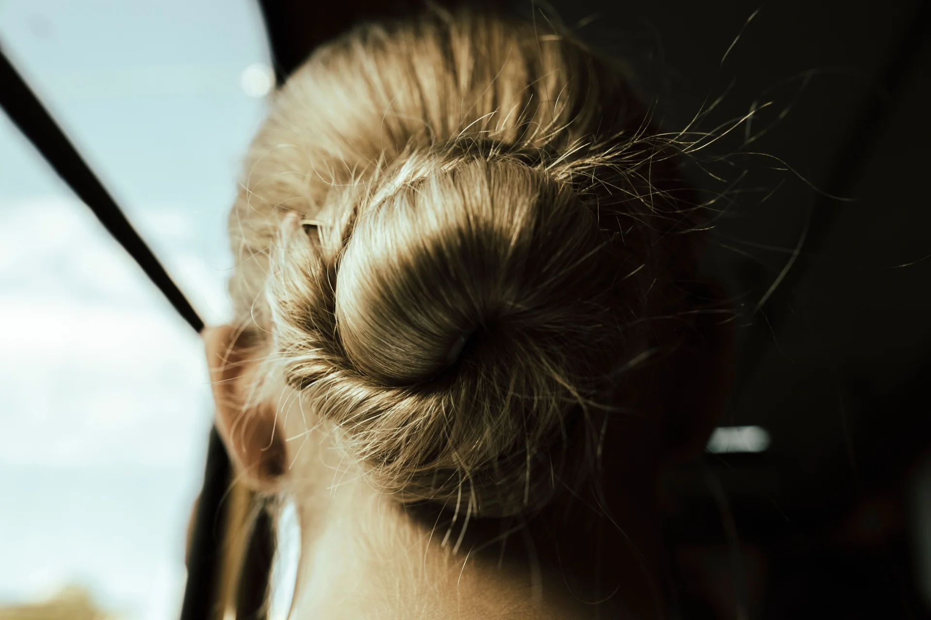 Zbliżenie na blond kok włosów, oświetlony promieniami słońca, podkreślający elegancję.